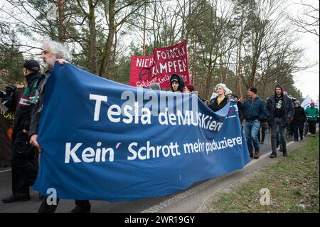 10 mars 2024, Brandebourg, Grünheide : lors d'une manifestation contre l'expansion de Tesla sous le slogan 'Tesla No Thanks!', les participants portent une bannière avec l'inscription 'Tesla deMUSKieren - Kein Schrott mehr produzieren'. Photo : Christophe Gateau/dpa Banque D'Images