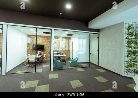 La personne est immergée dans une tâche dans un bureau élégant avec des murs de verre transparents. Le design moderne comprend la brique apparente, un moniteur élégant, confortable Banque D'Images