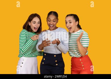 Copines excitées regardant l'écran du smartphone et faisant des gestes Banque D'Images