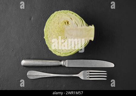 Chou blanc dans une coupe, fourchette et couteau sur une table en pierre noire Banque D'Images