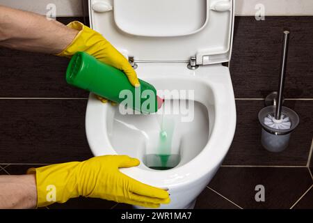 Nettoyage et désinfection des toilettes. Un nettoyant portant des gants de protection jaunes en caoutchouc traite les toilettes avec un agent nettoyant Banque D'Images