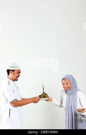 Deux musulmans asiatiques tenant une plaque blanche avec Ketupat pour la célébration de l'Aïd Al Fitr, isolés sur blanc Banque D'Images