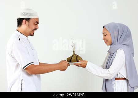 Asiatique musulman féminin et masculin tenant une assiette blanche avec Ketupat pour la célébration de l'Aïd Moubarak, isolé sur blanc Banque D'Images