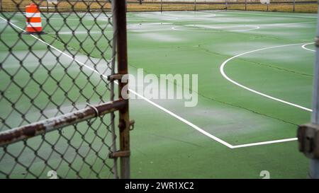 Terrain de basket-ball vert extérieur vide avec des fissures visibles et des lignes blanches le terrain attend les joueurs sur ce qui semble être un jour couvert, Banque D'Images