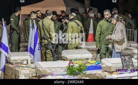 Jérusalem, Israël. 10 mars 2024. Les gens près de la tombe fraîche de Michael Gal qui a été tué dans la guerre de l'épée de fer entre Israël et le Hamas dans le regard. La photo présente une jeune fille civile enlacée par un soldat, ils se tiennent debout parmi les tombes. En arrière-plan, de nombreux soldats armés crédit : Yoram Biberman/Alamy Live News. Banque D'Images
