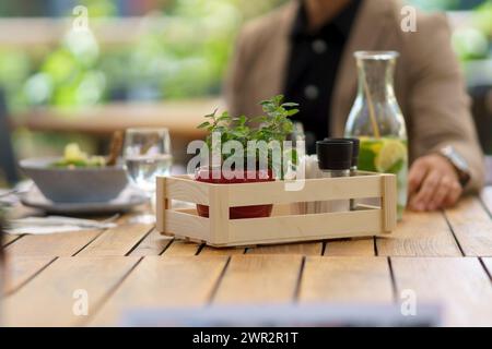 Table en bois sur le patio du restaurant. Table à manger avec du sel, des épices, des récipients d'assaisonnement en caisse, petite plante comme décoration. Banque D'Images