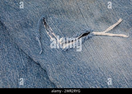 Trou déchiré dans un Jean denim. Concept de réparation et d'entretien des vêtements et pantalons de travail en denim. Banque D'Images