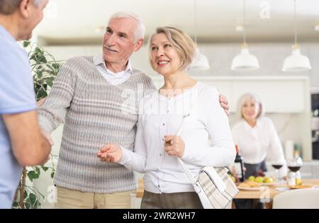 Deux couples de personnes âgées se accueillent chaleureusement alors qu'ils se réunissent pour un dîner festif de vacances à la maison Banque D'Images