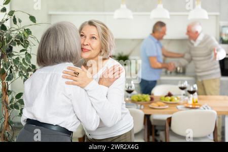 Deux femmes âgées se saluent en s'embrassant sur la joue. Pendant que les hommes se serrent la main Banque D'Images