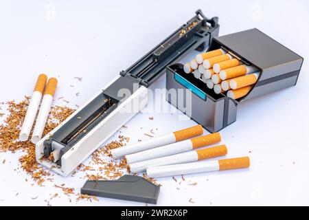 Machine à bourrer pour boyaux de cigarettes remplis de tabac, cigarettes vides sur fond blanc, étui à cigarettes avec des cigarettes maison. Banque D'Images