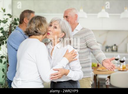Deux femmes âgées se saluent en s'embrassant sur la joue. Pendant que les hommes se serrent la main Banque D'Images