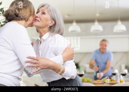 Deux femmes âgées se saluent en s'embrassant sur la joue. Pendant que les hommes se serrent la main Banque D'Images