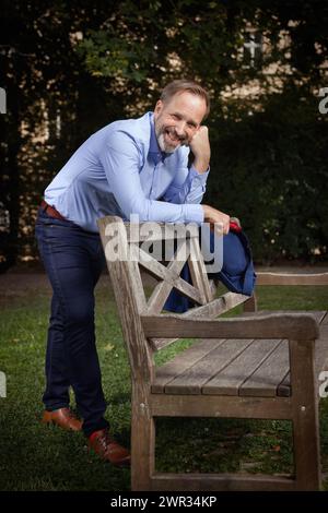 Homme en costume bleu avec chemise et cravate posant sur le banc dans le parc d'été Banque D'Images