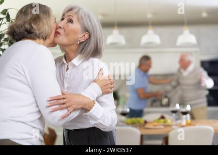 Deux femmes âgées se saluent en s'embrassant sur la joue. Pendant que les hommes se serrent la main Banque D'Images