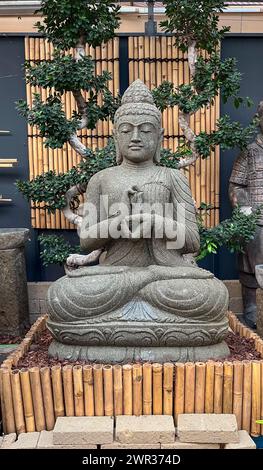 Figure de Bouddha en pierre assis dans un jardin intérieur avec un fond d'arbres orientaux et de bambou Banque D'Images