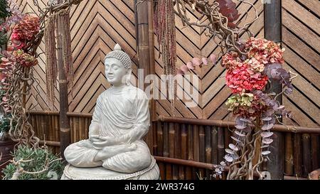 Figure de Bouddha en pierre assis dans un jardin intérieur avec un fond d'arbres orientaux et de bambou Banque D'Images