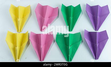 Avions en papier alignés en rose, violet, vert et jaune isolés sur un fond blanc Banque D'Images