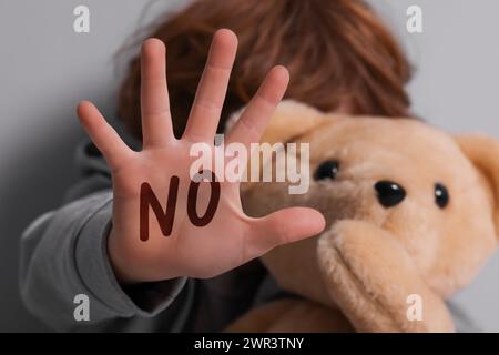 Maltraitance des enfants. Garçon avec jouet faisant un geste d'arrêt près du mur gris, mise au point sélective. Non écrit sur sa main Banque D'Images