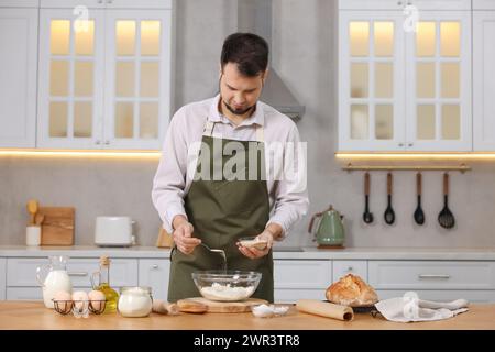 Faire du pain. Homme mettant la levure sèche dans un bol avec de la farine à la table en bois dans la cuisine Banque D'Images