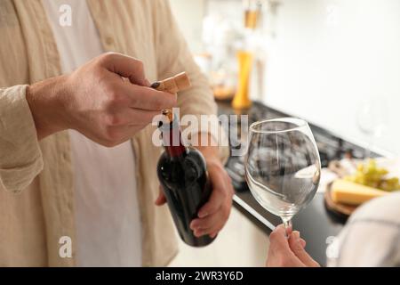 Homme ouvrant bouteille de vin avec tire-bouchon tandis que femme tenant verre à vin à l'intérieur, gros plan Banque D'Images