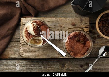 Délicieux tiramisu dans des verres, des cuillères et des grains de café sur une table en bois, vue de dessus Banque D'Images