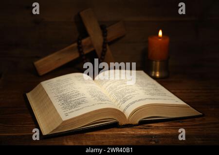 Bible, croix, perles de chapelet et bougie d'église sur table en bois Banque D'Images