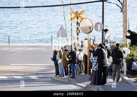 Les touristes prennent des photos autour du passage à niveau de la gare Kamakura Kokomae d'Enoden dans la ville de Fujisawa, préfecture de Kanagawa, le 28 février 2024. Ce passage à niveau est présenté dans la célèbre série d'animation japonaise 'Slam Dunk'. C'est une destination touristique populaire pour les touristes nationaux et étrangers à visiter et à prendre des photos. Cependant, en raison du grand nombre de touristes visitant le train d'Enoden est devenu extrêmement fréquenté, et les résidents vivant le long de la ligne ont été touchés par le problème du surtourisme. Crédit : Yosuke Tanaka/AFLO/Alamy Live News Banque D'Images