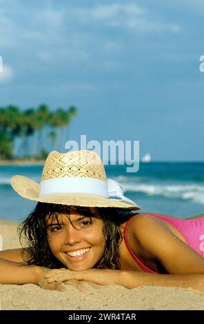 porto rico porto rico cheveux noirs jolie jeune femme portrait souriant caméra frontale avec chapeau de paille palmier bacground plage tropicale Banque D'Images