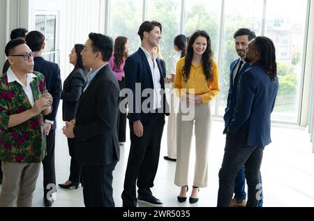 Un groupe de personnes se tient debout dans une pièce, certaines portant des costumes et des cravates. Ils sourient tous et semblent profiter de la compagnie de l'autre. Banque D'Images