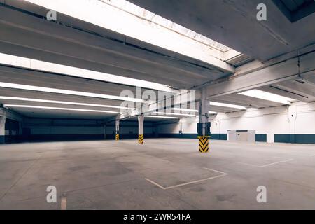 Intérieur d'un entrepôt industriel vide spacieux ou d'un parking. Piliers en béton avec un panneau d'avertissement noir et jaune rayé Banque D'Images