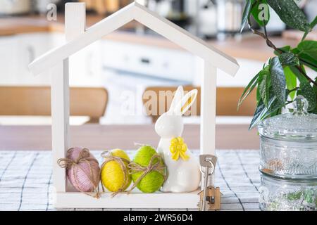 Clé et minuscule maison de maison confortable avec décor de Pâques avec lapin et oeufs sur la table de la cuisine. Bâtiment, conception, projet, déménagement à la nouvelle maison, hypothèque, Banque D'Images