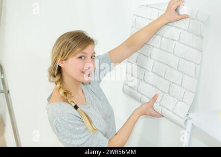 Woman putting up wallpaper Banque D'Images