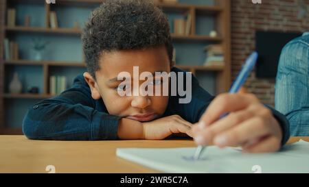 Triste bouleversé paresseux non motivé fatigué épuisé fatigué petit élève afro-américain écolier écriture notes écrire des devoirs allongé sur la table. Ethnique Banque D'Images