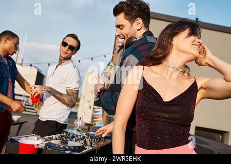 joyeuse femme aux cheveux longs faisant la fête à côté de ses amis multiraciaux joyeux sur le toit Banque D'Images