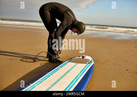 Un surfeur de sexe masculin attachant la laisse de planche de surf à sa cheville Banque D'Images