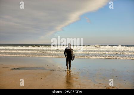 Un surfeur marchant vers la mer à Good Harbor Beach à Gloucester, ma Banque D'Images