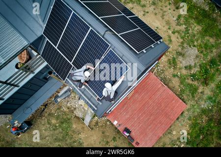 Installateurs construisant la station de module solaire photovoltaïque sur le toit de la maison. Hommes électriciens dans les casques installant le système de panneau solaire à l'extérieur. Concept d'énergie alternative et renouvelable. Vue aérienne. Banque D'Images