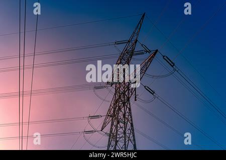 Pylône métallique transportant de l'électricité haute tension avec un ciel bleu et rouge, couleurs de l'aube. France, Europe Banque D'Images