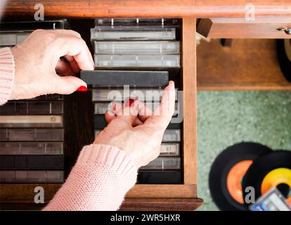 Senior choisissant des cassettes sur des meubles en bois. Banque D'Images