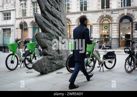 Les employés de la ville passent devant la sculpture intitulée « City Wing » et les vélos de location Lime sur Threadneedle Street dans la ville de Londres, le quartier financier de la capitale (alias Square Mile), le 7 mars 2024, à Londres, en Angleterre. 'City Wing' est de l'artiste Christopher le Brun. La sculpture en bronze de dix mètres de haut a été réalisée par Christopher le Brun, président de la Royal Academy of Arts, commandé par Hammerson en 2009. Elle est appelée « The City Wing » et a été moulée par Morris Singer Art Founders, réputée être la plus ancienne fonderie d’art au monde. Banque D'Images