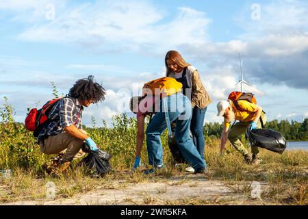 Cette image inspirante capture un groupe d'amis soucieux de l'environnement, de diverses origines ethniques, y compris caucasiennes et noires, participant à un nettoyage des rives du lac. Chaque personne est activement engagée dans la collecte des ordures, démontrant son engagement à préserver la beauté naturelle du paysage. La présence d'éoliennes en arrière-plan fait allusion à une communauté qui valorise la durabilité et les énergies renouvelables. Les amis sont habillés dans une tenue décontractée, adapté au travail en plein air, et le ciel clair ci-dessus reflète la positivité de leur impact sur l'environnement. Ragoût environnemental Banque D'Images