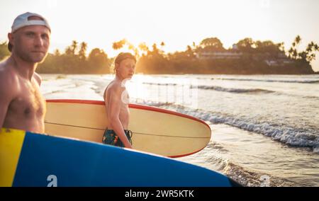 Un jeune garçon avec une planche de surf va à la mer de surf. Il a des vacances d'hiver et profiter d'un beau coucher de soleil avec son père sur l'île du Sri Lanka. Banque D'Images