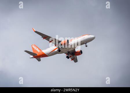 Un avion EasyJet, peint dans des couleurs orange et blanc saisissantes, vole à travers la vaste étendue du ciel bleu Banque D'Images