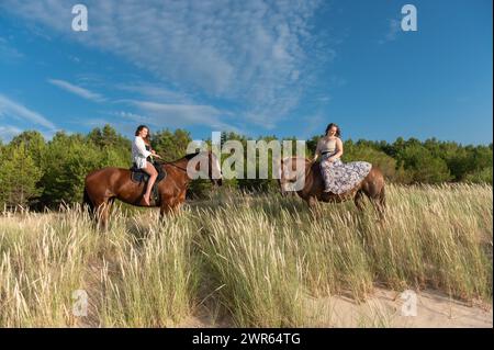 Deux femmes à cheval sur une plage près d'une forêt Banque D'Images
