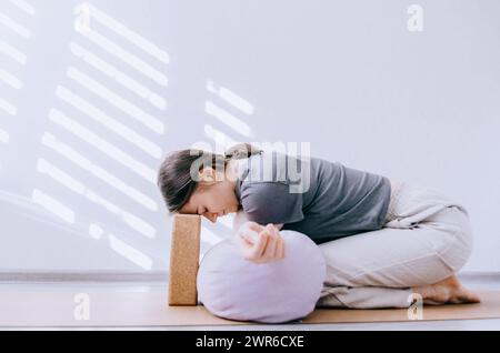 Femme dans des vêtements décontractés faisant le yin yoga bras croisé stretch avec traversin et bloc de liège Banque D'Images