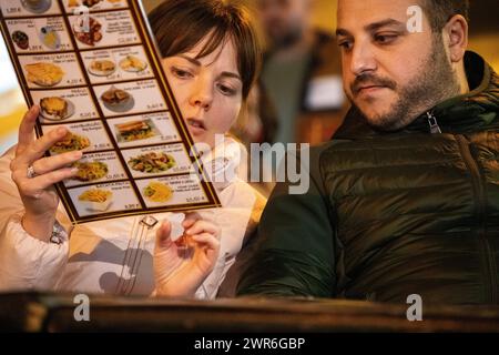 Dans un stand de restaurant confortable, deux amoureux porteront sur le menu, leur excitation partagée palpable alors qu'ils planifient leur repas ensemble Banque D'Images