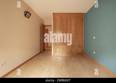 Une chambre vide avec des murs crème et vert avec une armoire encastrée à quatre sections avec des portes en bois clair Banque D'Images