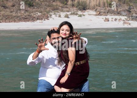 Amour et rire, Une femme heureuse est assise sur ses genoux, amusée par son geste d'horreur ludique devant le gange à Rishikesh Banque D'Images