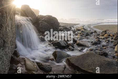 Un courant d'eau coule entre de grands rochers sur une plage. L'eau est claire et calme, et les rochers sont dispersés dans toute la scène Banque D'Images