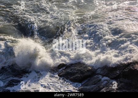 Une grosse vague s'écrasant contre un rivage rocheux. L'eau est blanche et mousseuse, et les rochers sont dispersés dans toute la scène. La scène est puissante et le dr. Banque D'Images